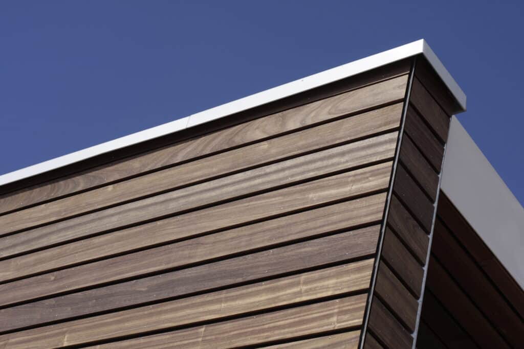 Façade bois moderne et design sous un ciel bleu éclatant Façade moderne en bois lambrissé avec des clins bruns foncés et des fixations claires, sous une garniture blanche et un ciel bleu.